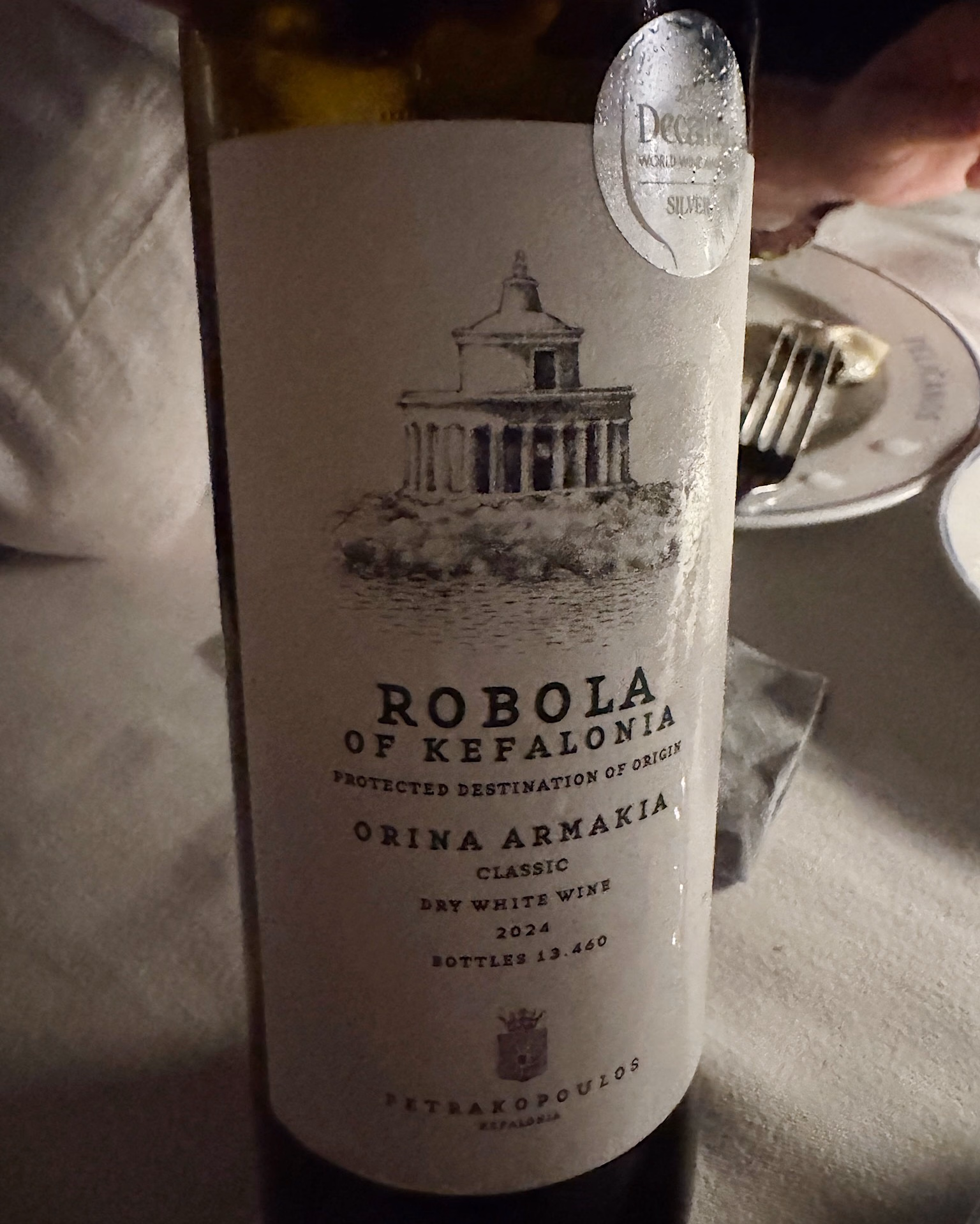 Bottle of Robola of Kefalonia dry white wine, Petrakopoulos 2024, with a silver Decanter award sticker, on a white tablecloth.