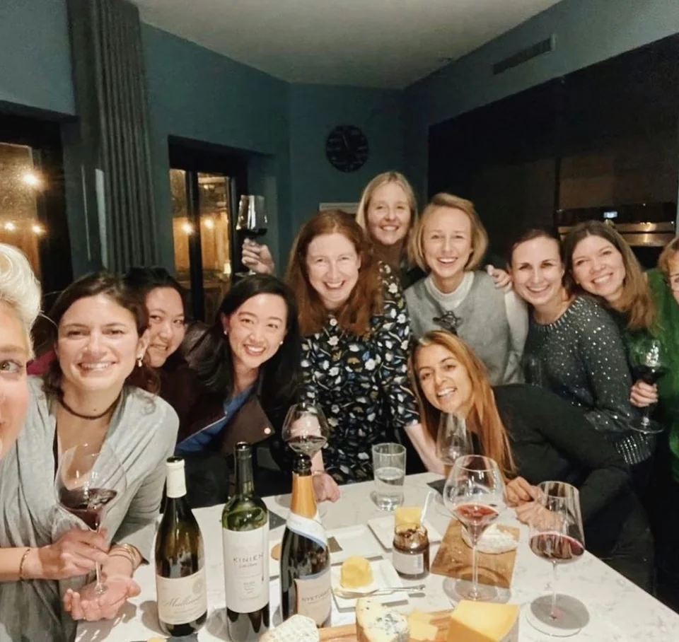 Group of women enjoying a wine tasting around a table with wine glasses, bottles and cheese