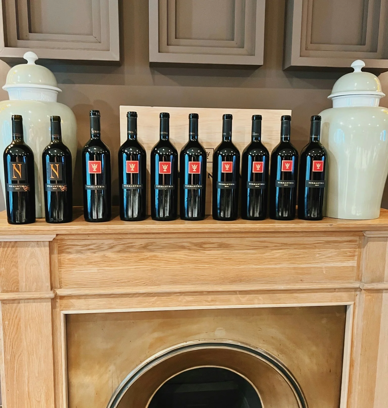 Row of Terramanthia wine bottles displayed on a wooden mantel above a fireplace