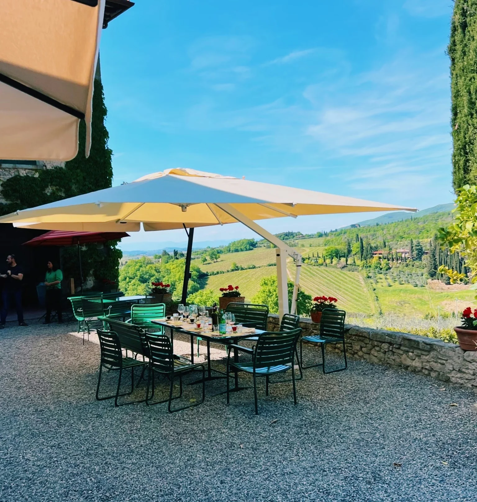 Outdoor terrace with tables, chairs and umbrellas overlooking Savignola's Tuscan vineyards and hills