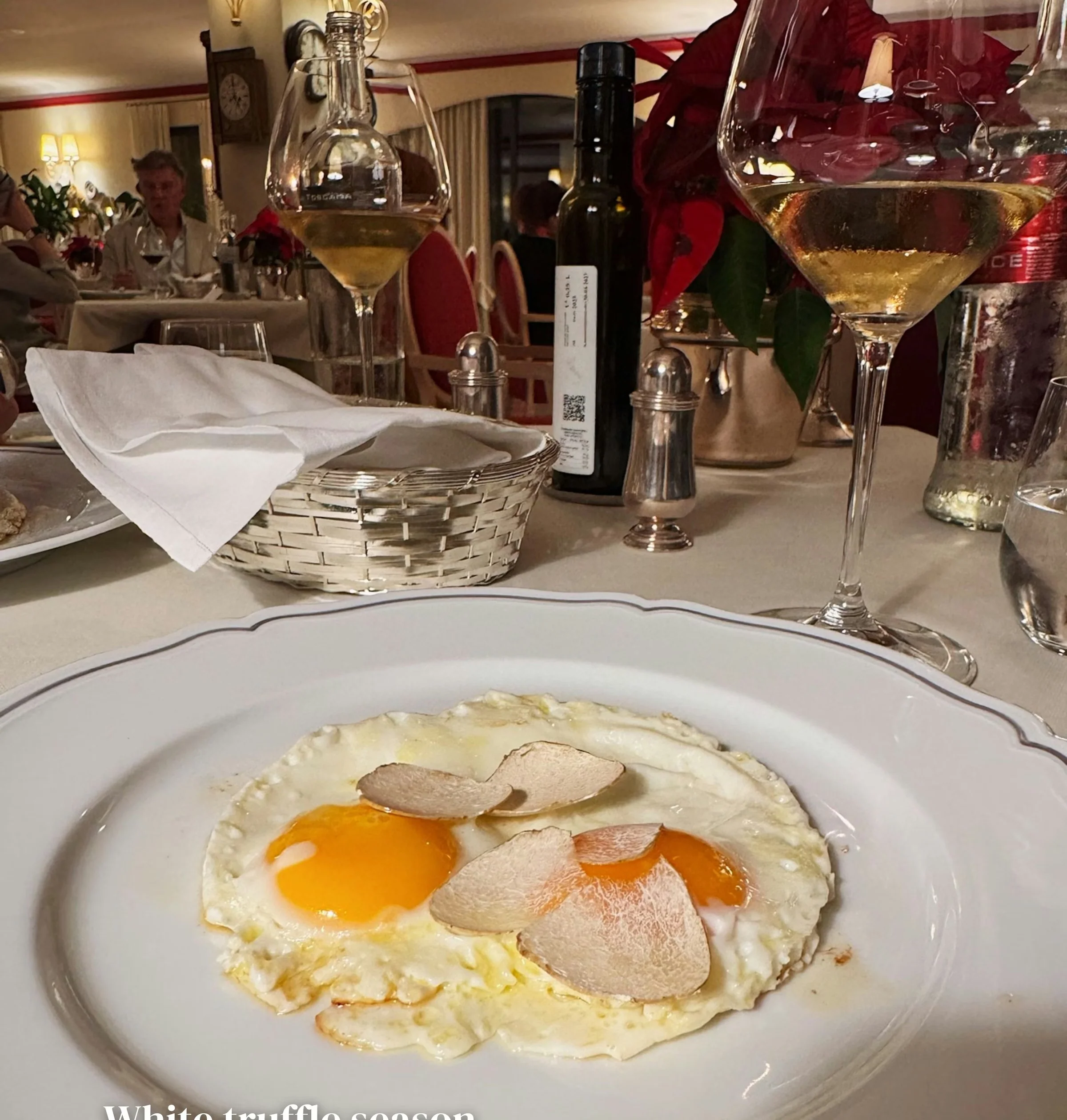Fried eggs topped with truffle beside wine glasses and bottles on a restaurant table