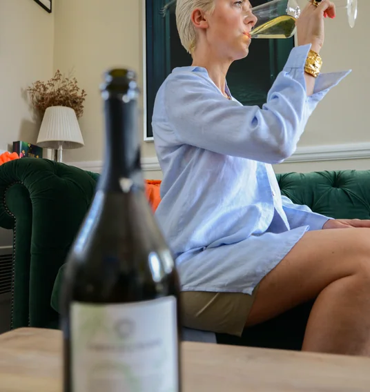 Woman drinking sparkling tea from a wine glass, with a bottle in the foreground