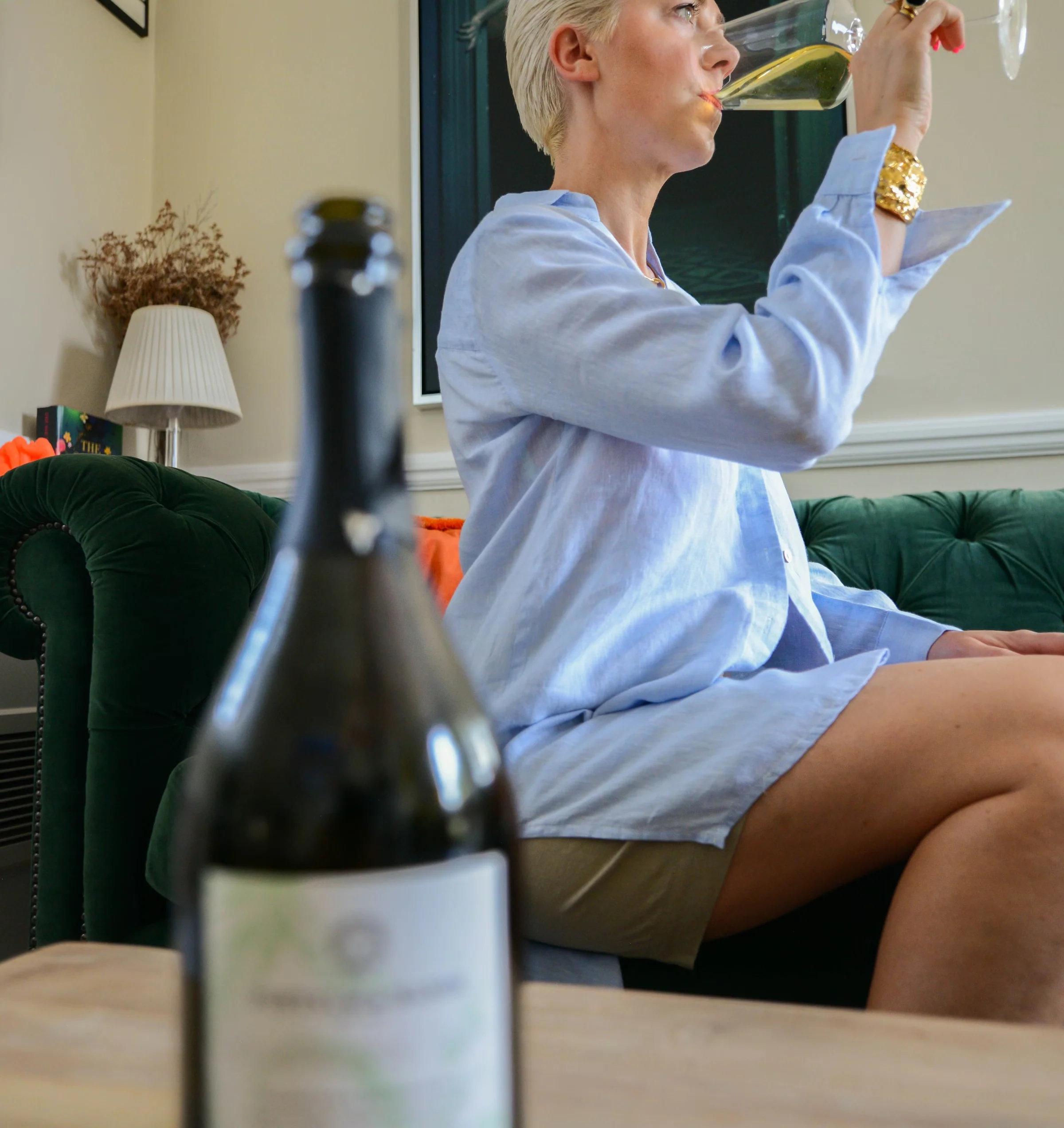Woman drinking sparkling tea from a wine glass, with a bottle in the foreground
