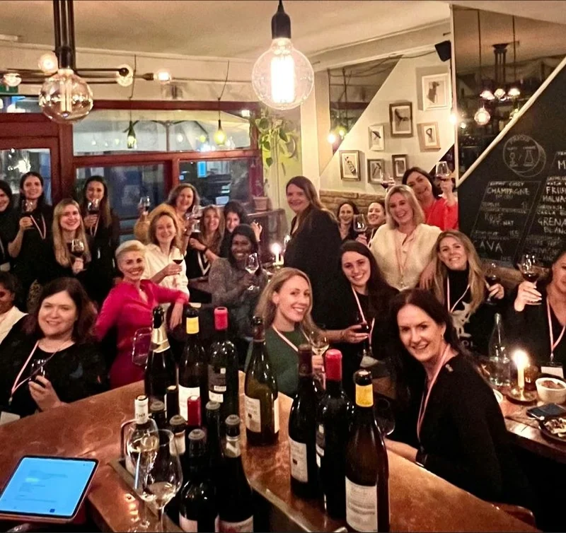 Group of women gathered around tables with wine bottles and glasses inside Lady of the Grapes