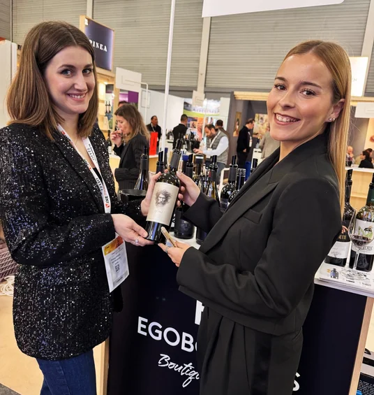 Elizabeth holds a wine bottle with a representative at the Ego Bodegas stand at Wine Paris.