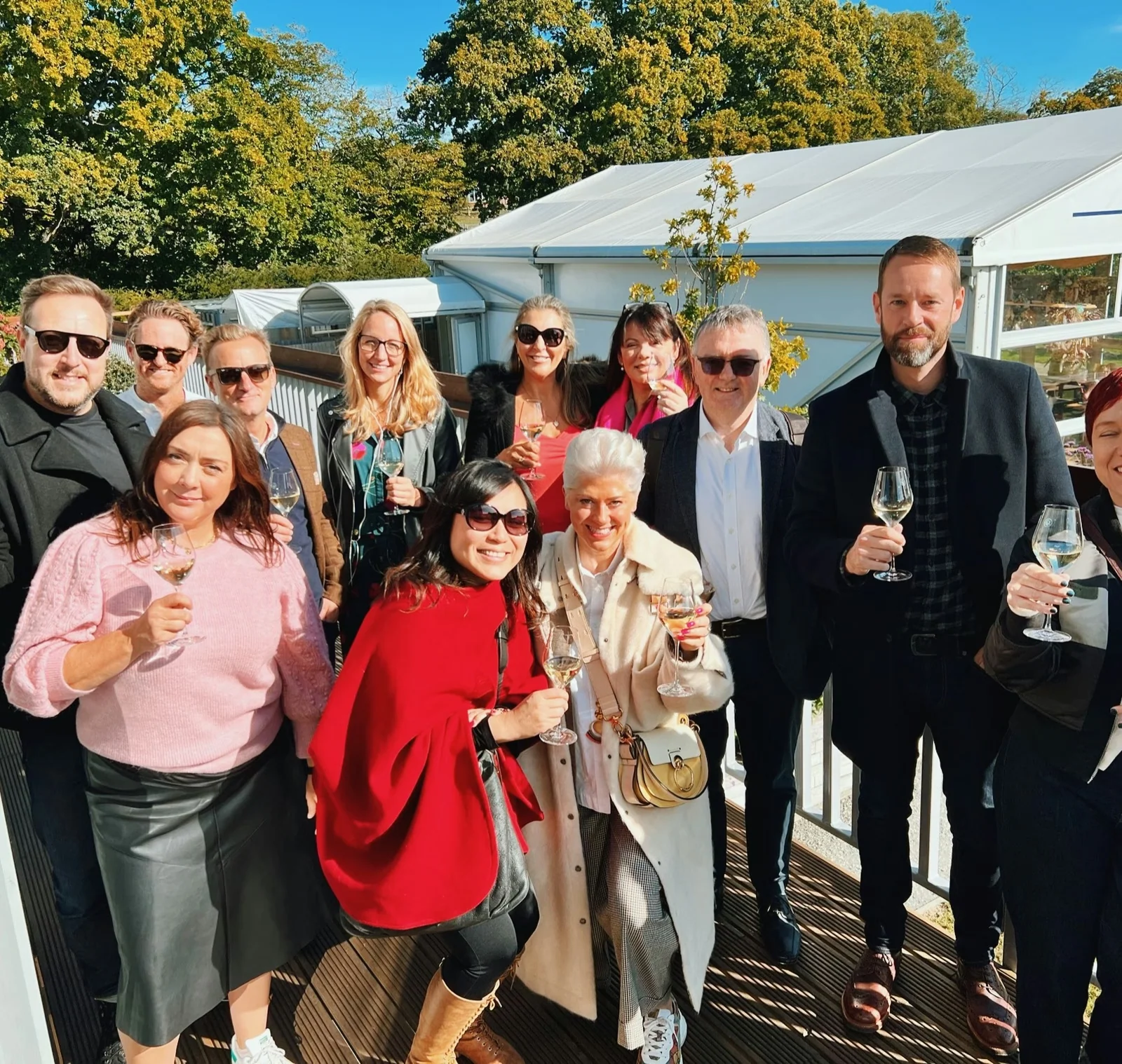 Group of people holding wine glasses outside a vineyard winery on a sunny autumn day