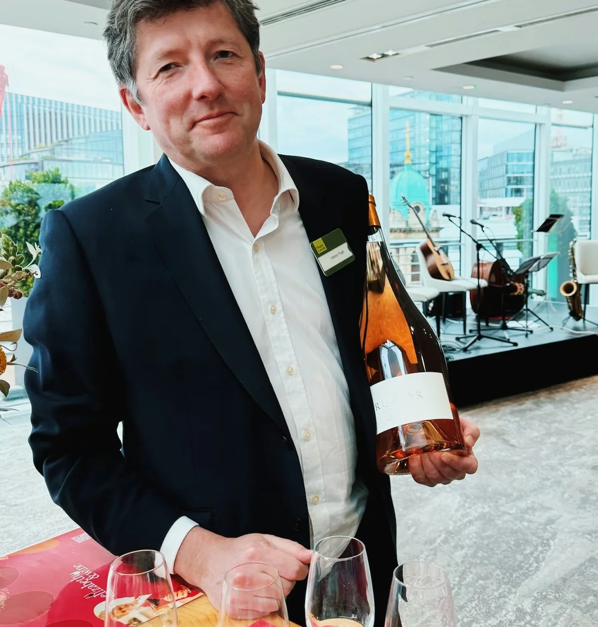 Man holding a large bottle of Ruinart rosé beside wine glasses at a corporate tasting