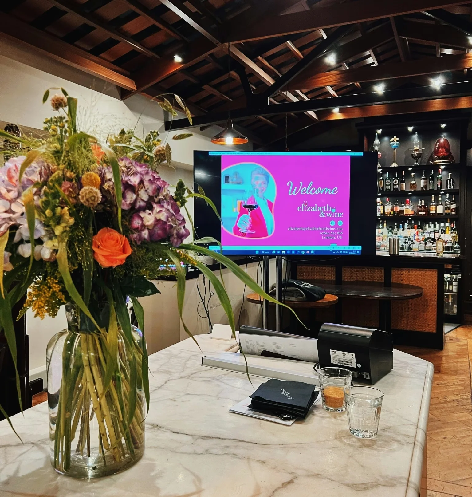 Marble bar with flowers and a screen displaying an Elizabeth & Wine welcome slide