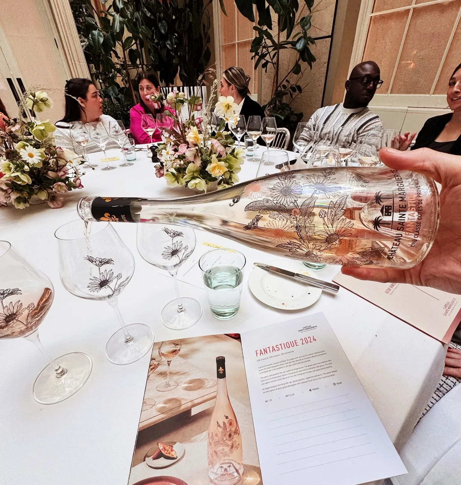 Rosé being poured at a floral dining table, with wine glasses, diners and a menu labelled Fantastique 2024