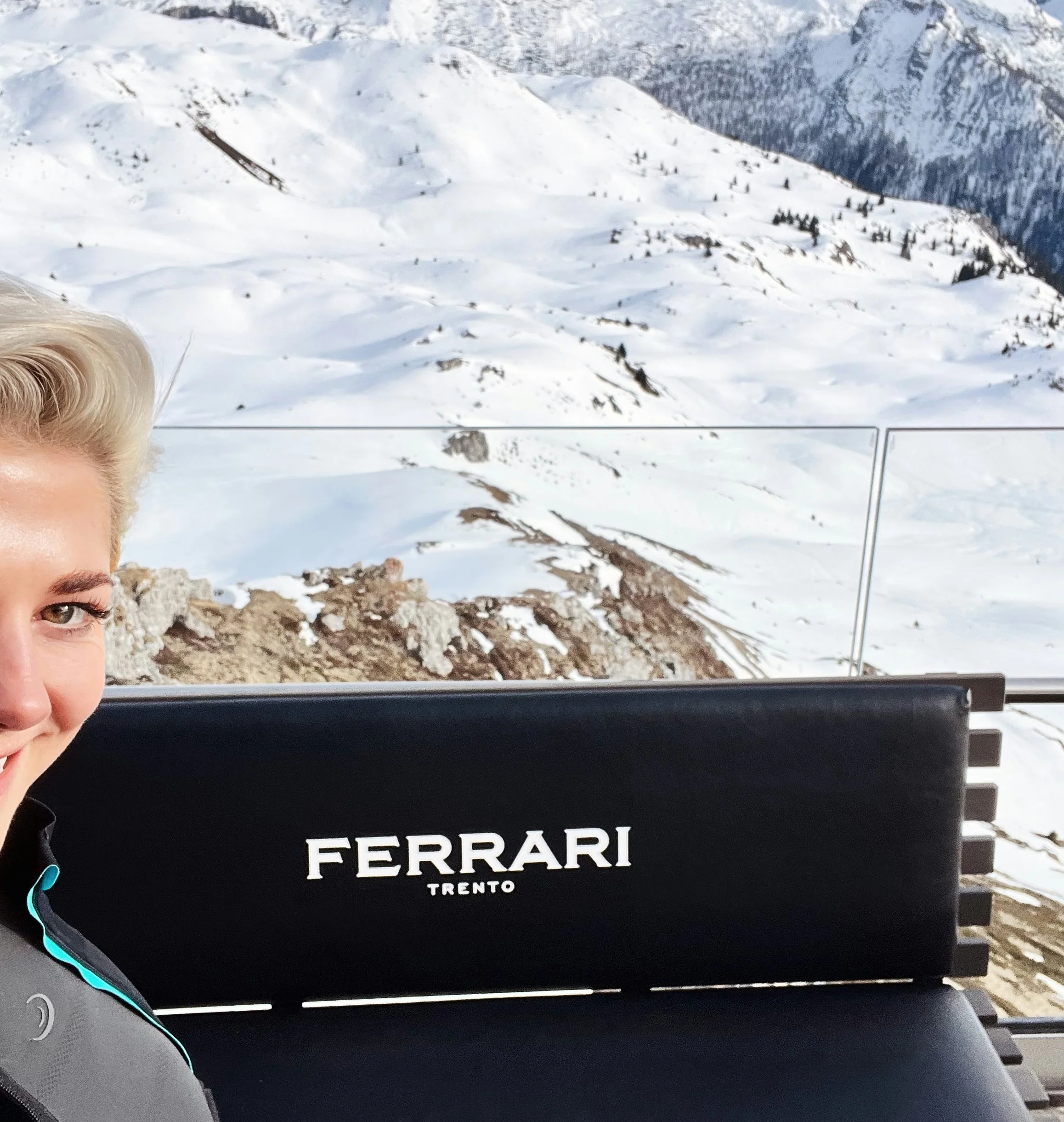 Elizabeth beside a Ferrari Trento seat overlooking snow-covered Dolomite mountains
