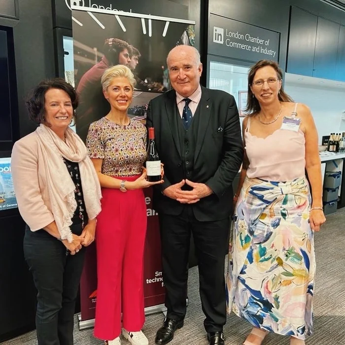Four people pose at London Chamber of Commerce and Industry, with one holding a bottle of wine.