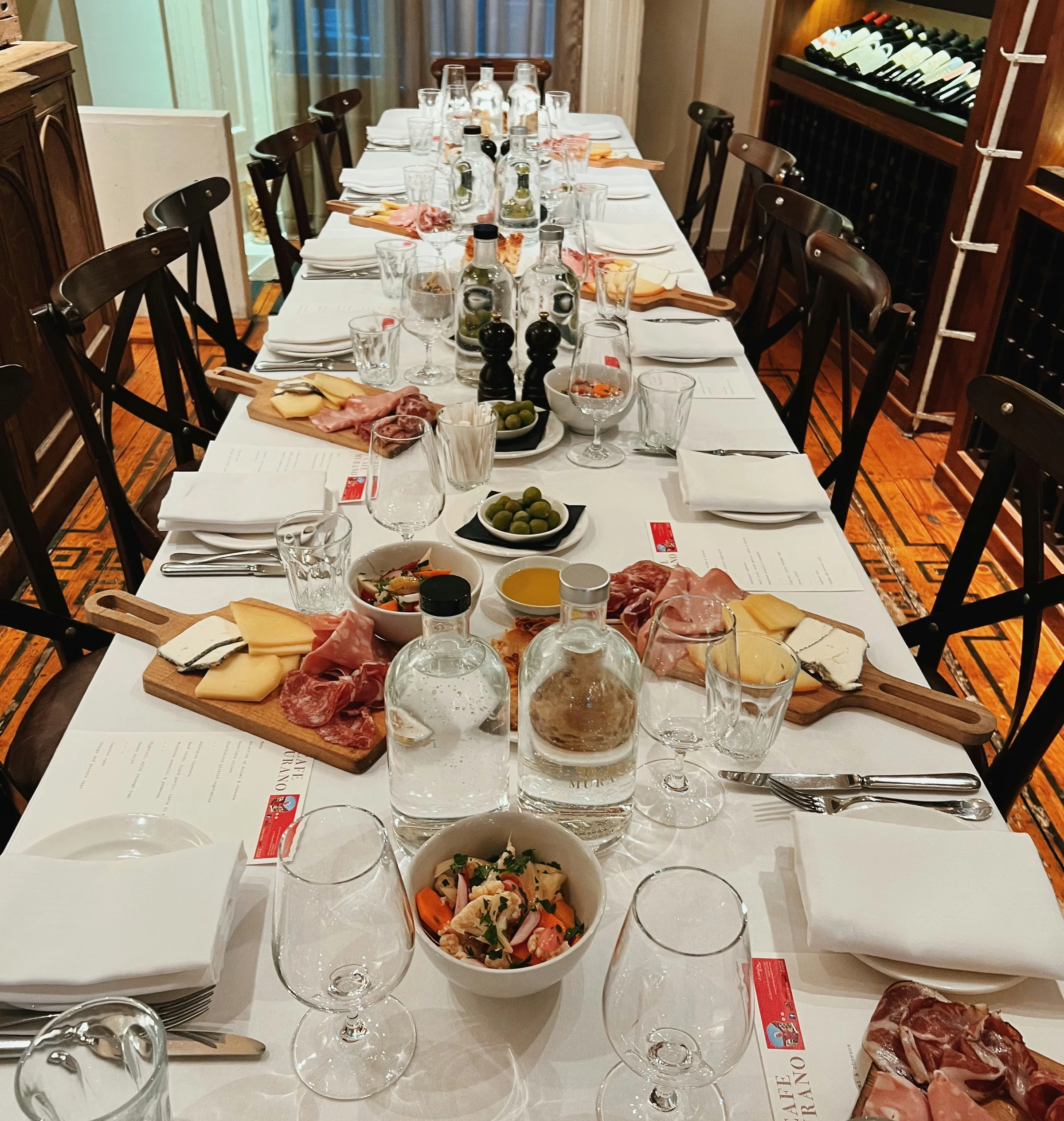 Long dining table set with wine glasses, bottles, sharing boards and a wall of wine