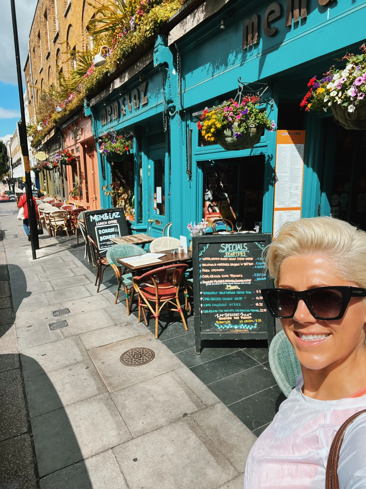 Woman taking selfie outside colourful flower-covered restaurant terrace
