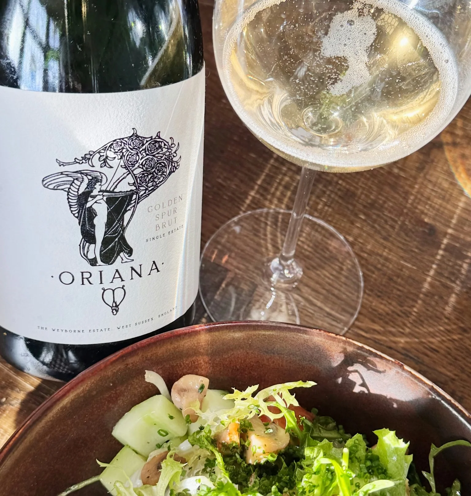 Oriana Golden Spur Brut beside a glass of sparkling wine and a fresh salad
