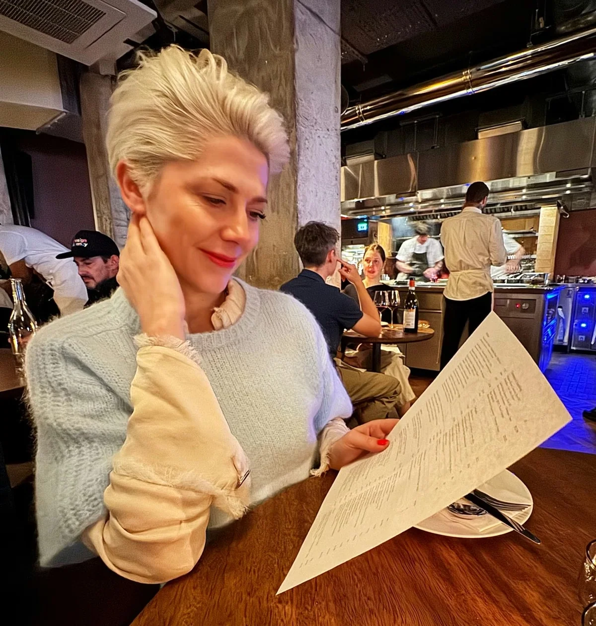 Diner reading a menu at a restaurant table beside an open kitchen