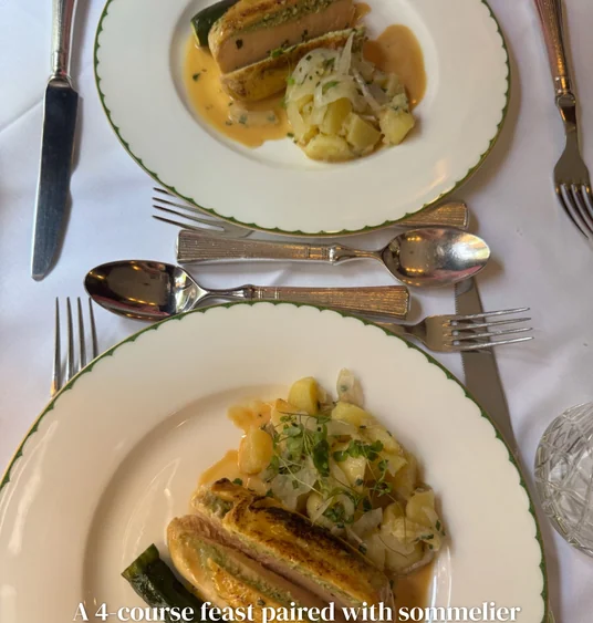 Two plated gourmet meals with vegetables and sauce on a formal white table setting