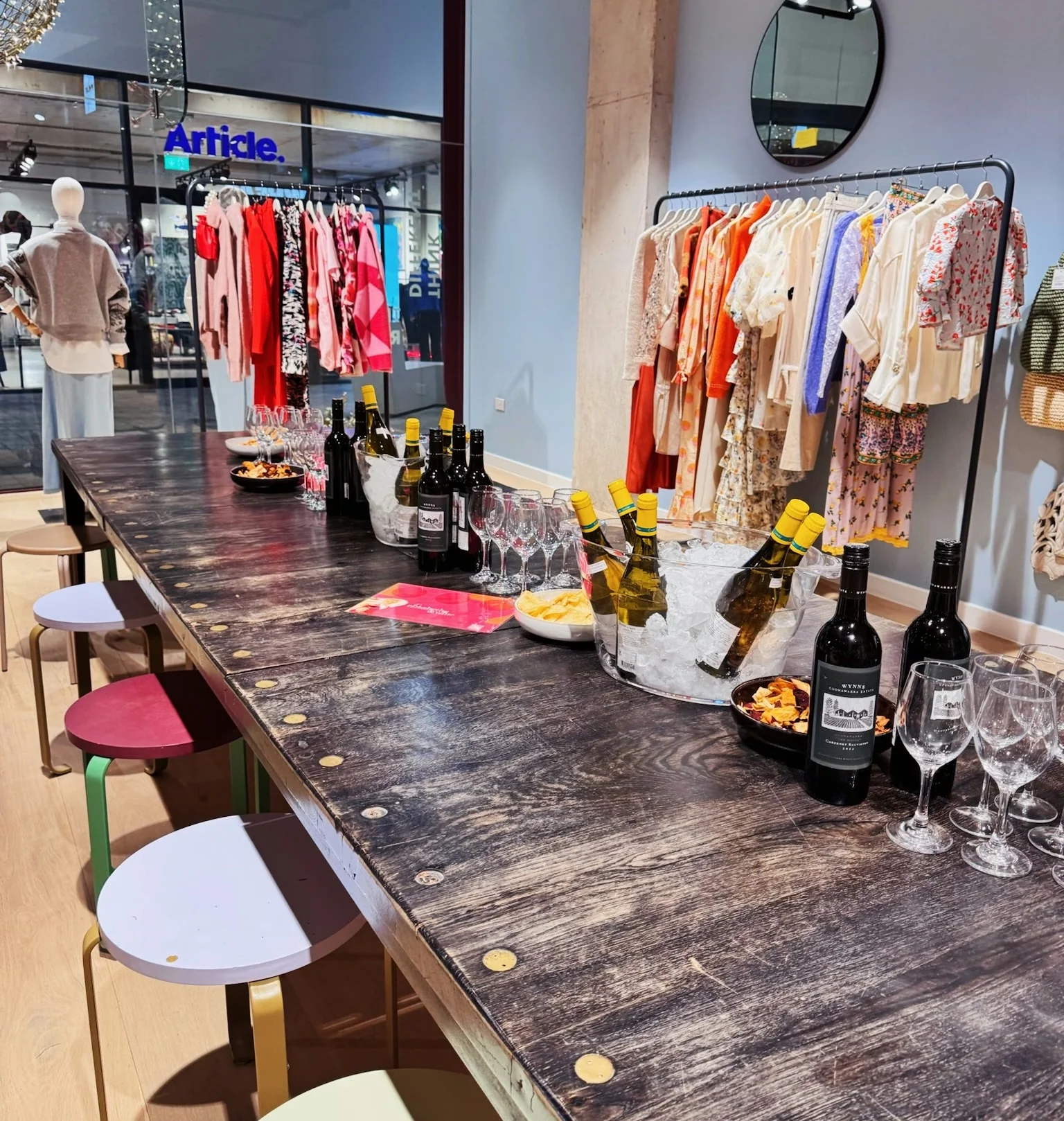 Wine tasting table set with bottles, glasses, ice buckets and snacks inside a clothing shop
