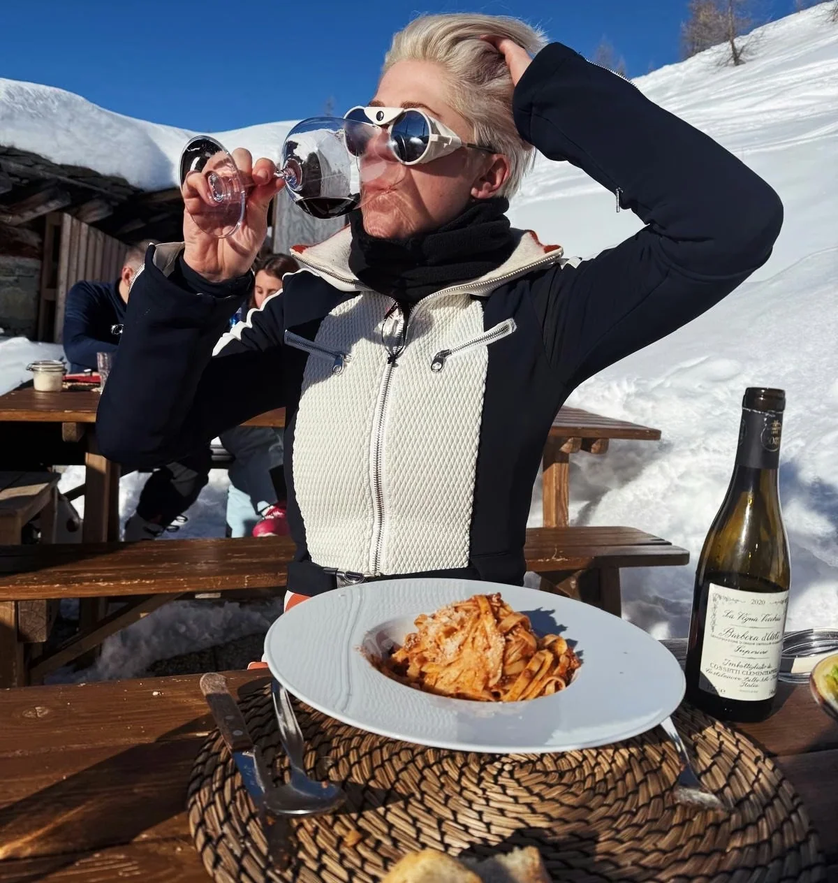 Diner drinking wine beside pasta and a bottle at an outdoor snowy restaurant in Champoluc