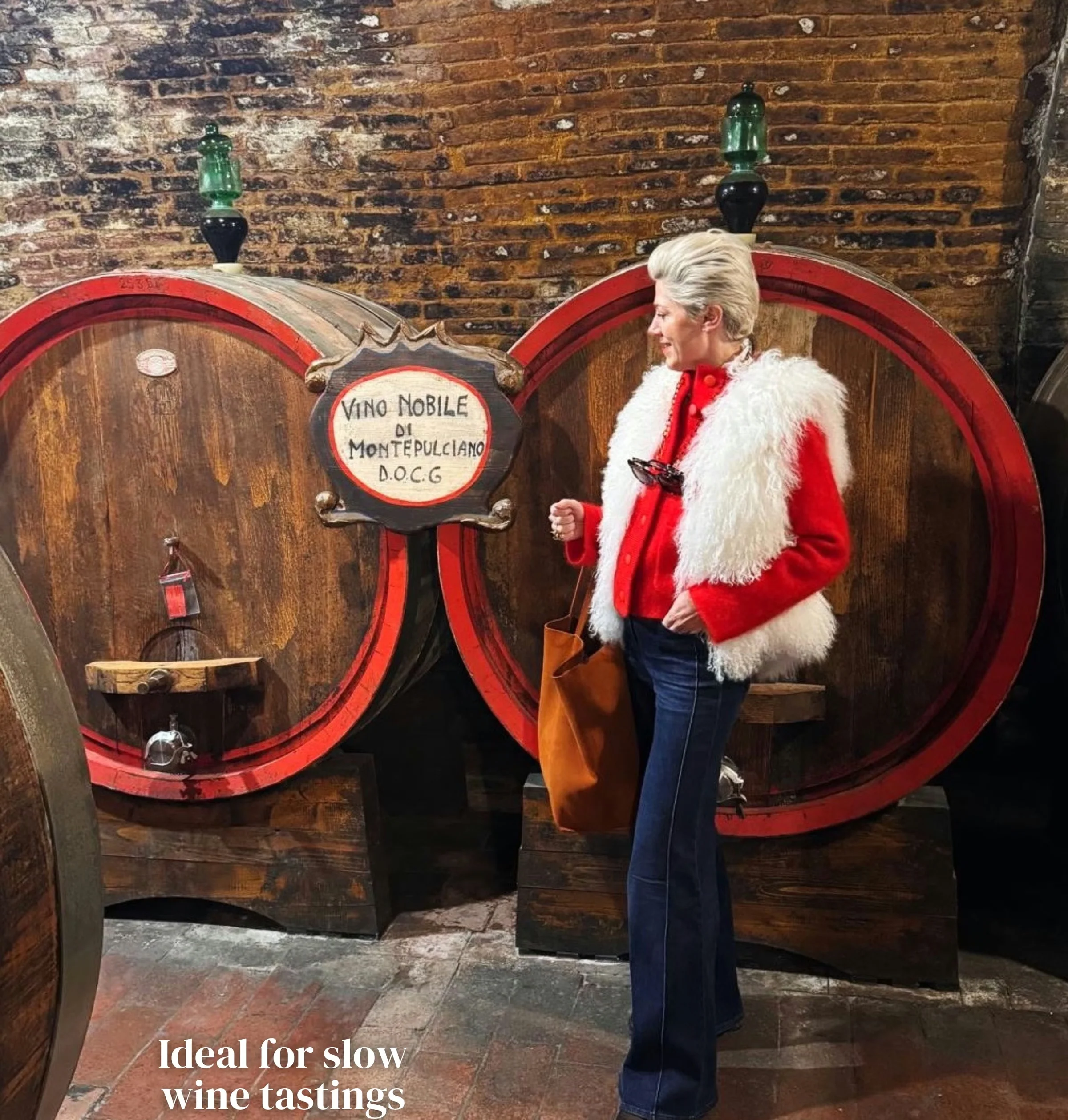 Woman in a red jacket standing beside large wine barrels in a Tuscan cellar