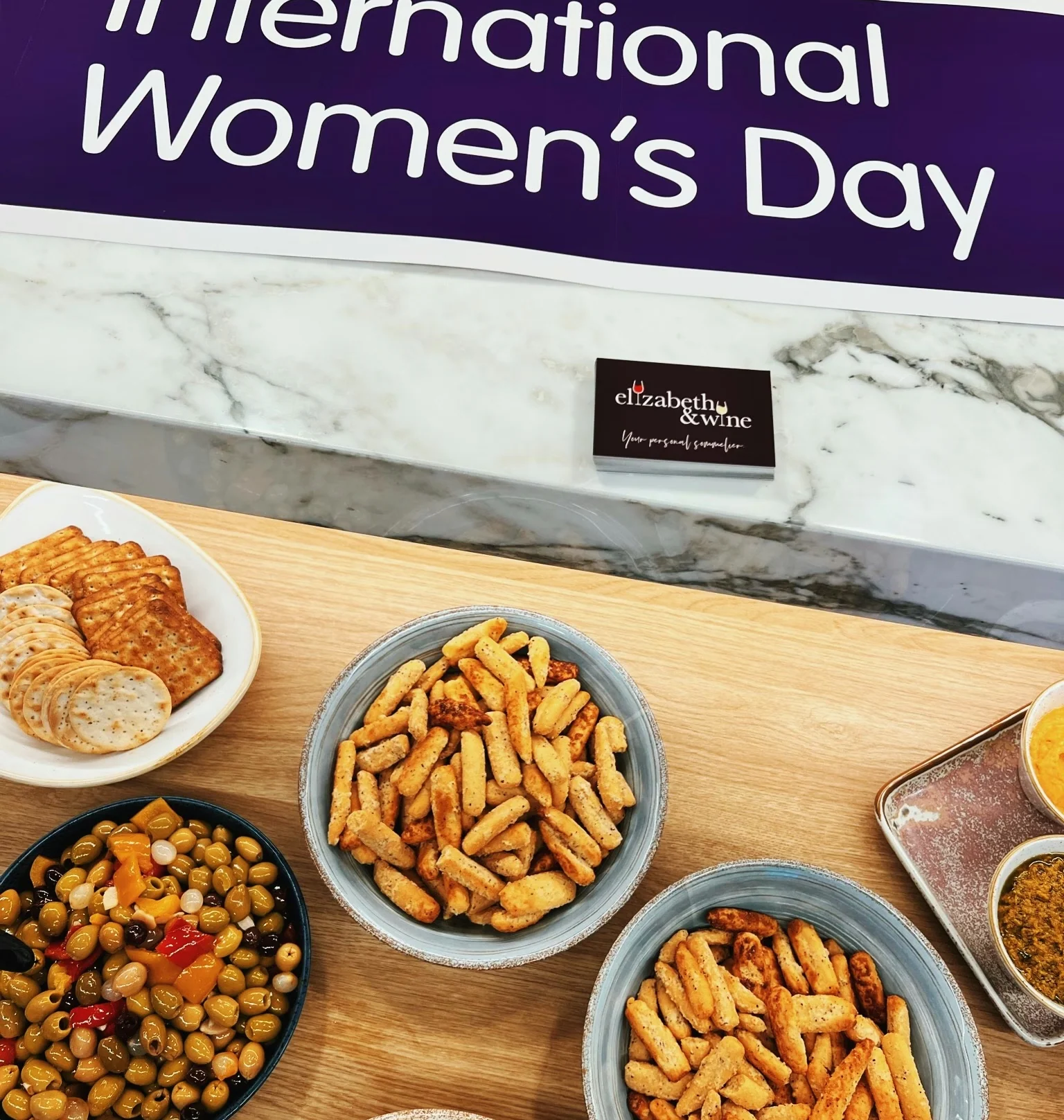 International Women's Day sign above a table of crackers, olives and dips