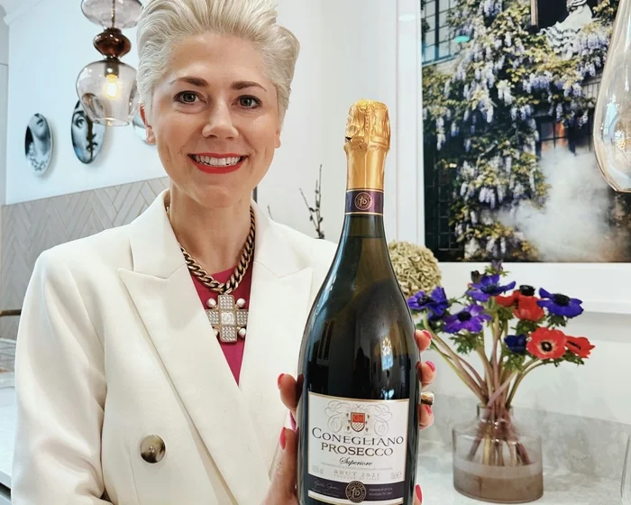 Smiling woman holding a bottle of Conegliano Prosecco indoors