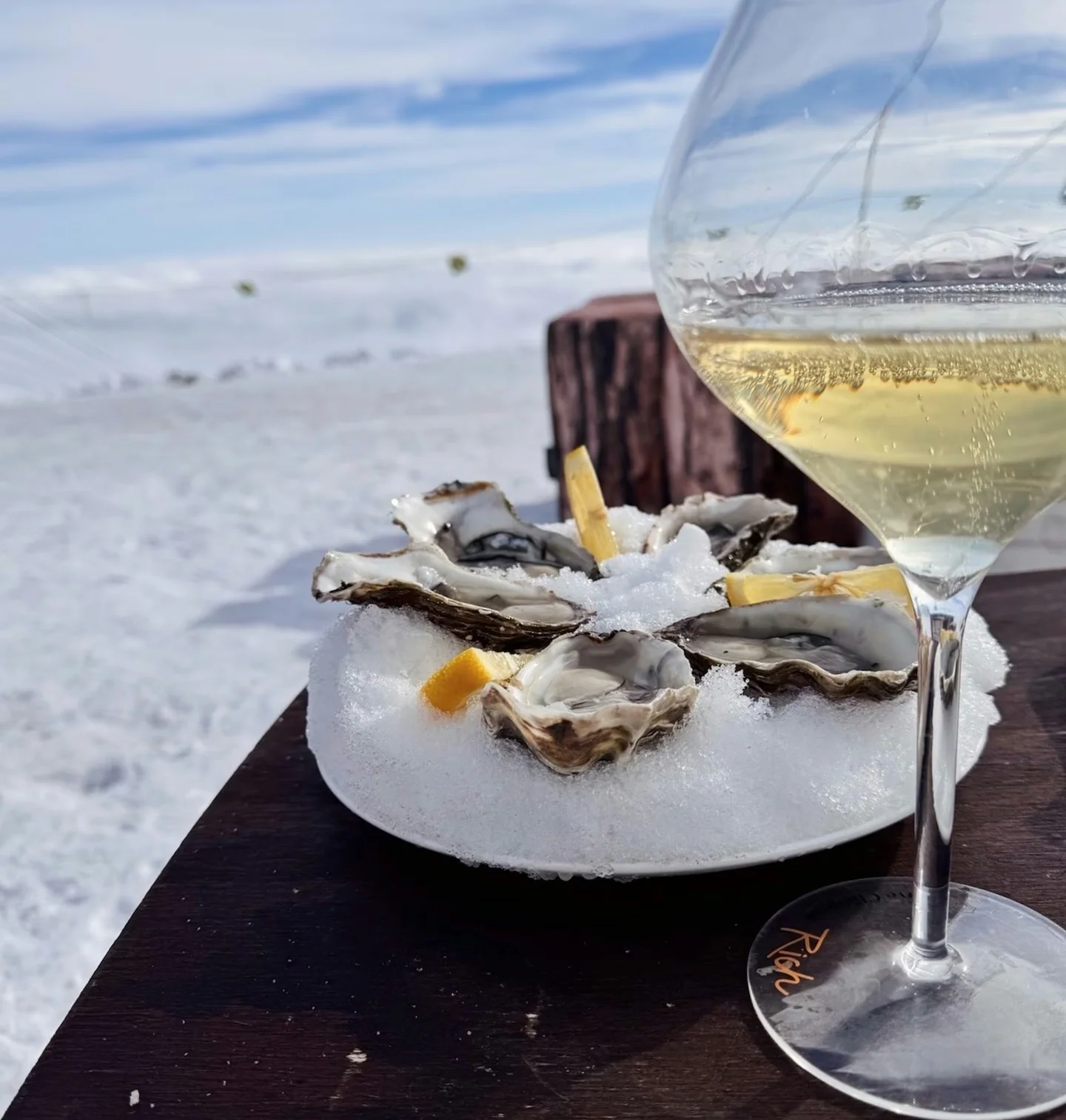 Glass of sparkling wine and oysters on ice beside a snowy mountain landscape
