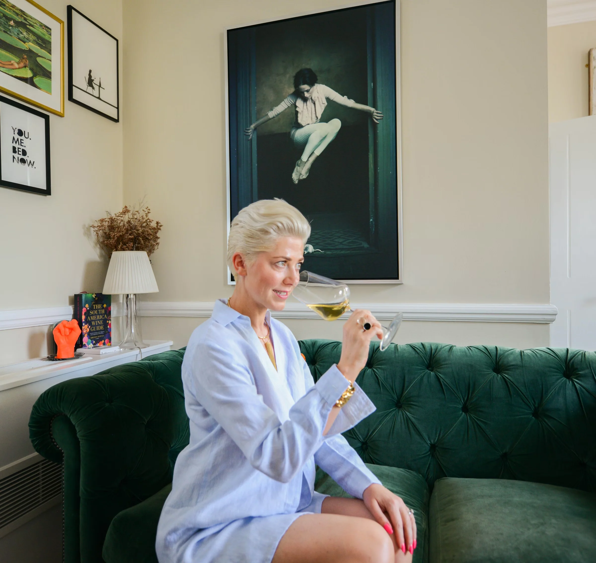 Woman holding a glass of sparkling tea while seated on a green velvet sofa in a sitting room