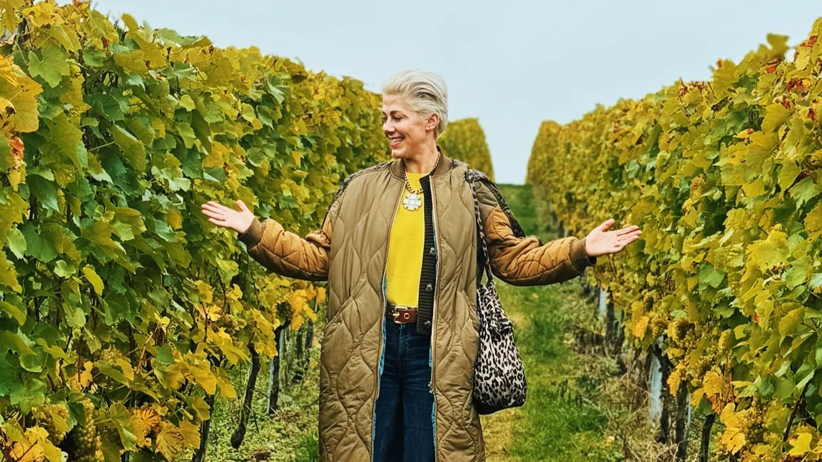 Woman standing between vineyard rows with arms outstretched