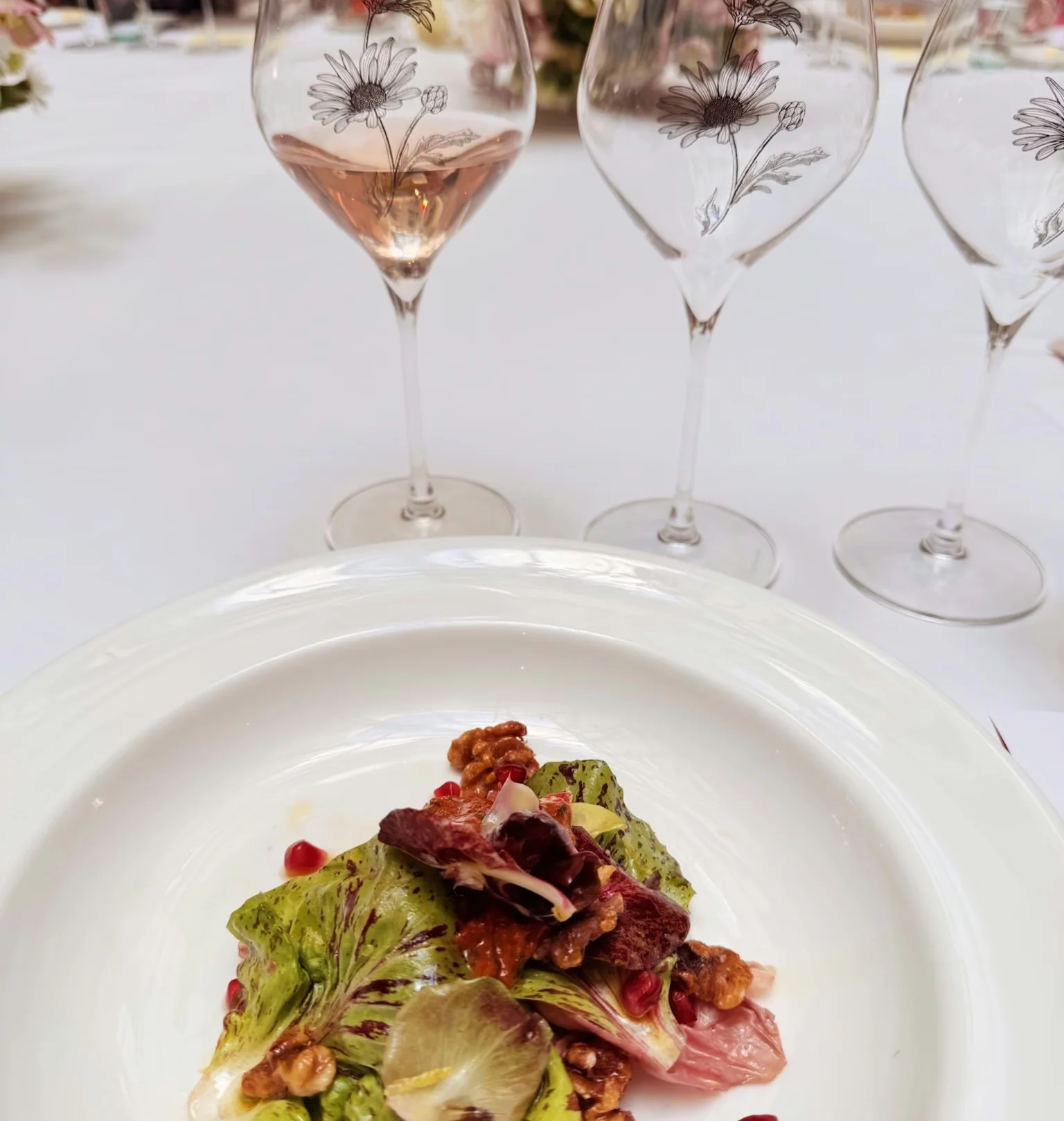 Rosé wine in flower-decorated glasses beside a plated salad with walnuts and pomegranate seeds