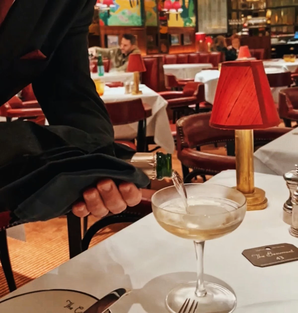 Sparkling wine being poured into a coupe in a colourful restaurant dining room