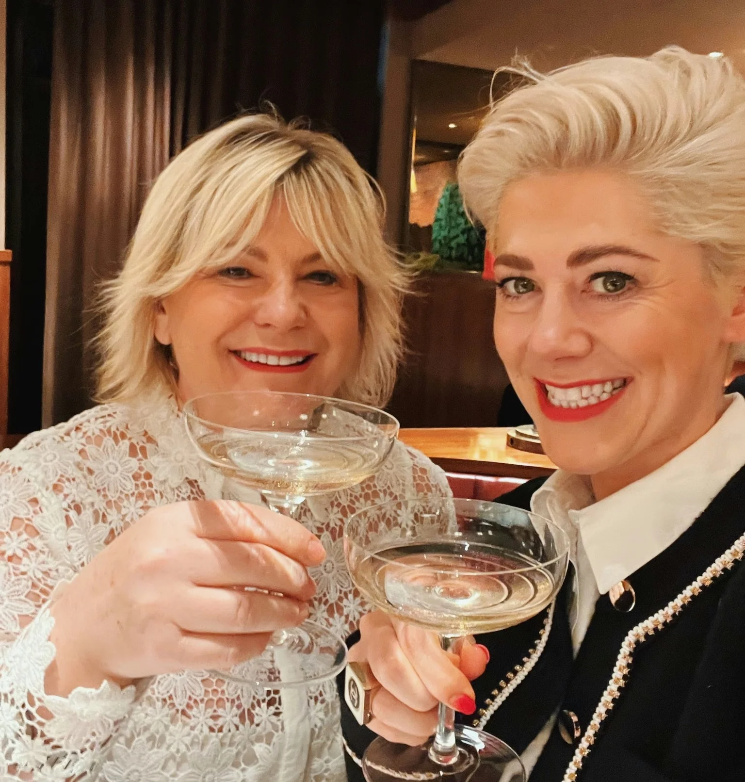 Two women smiling and raising coupe glasses in an elegant restaurant