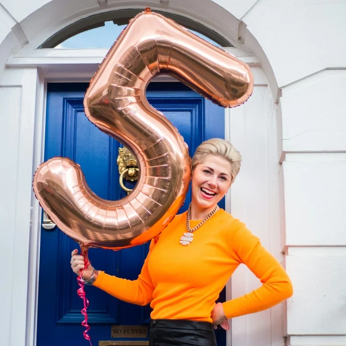 Woman holding rose gold number five balloon outside blue door