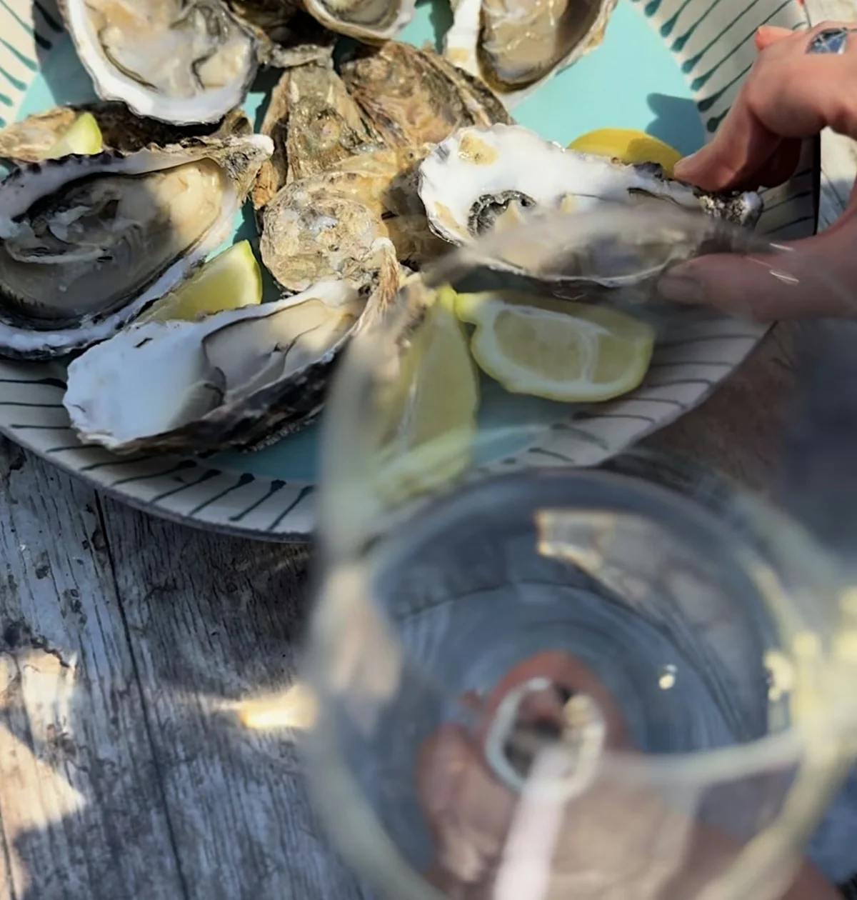 Fresh oysters with lemon on a plate beside a partially visible wine glass