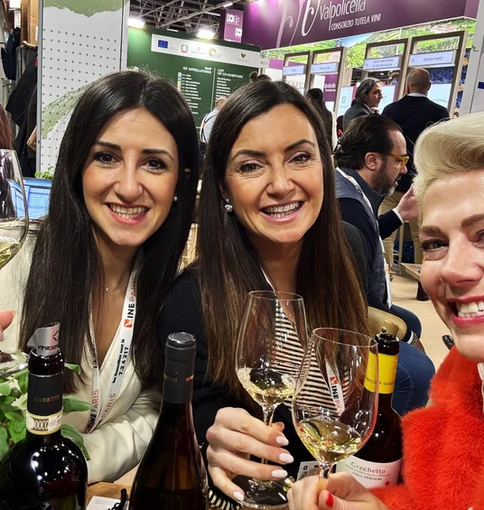 Elizabeth and two women pose with wine glasses at the Valpolicella stand at Wine Paris 2025.
