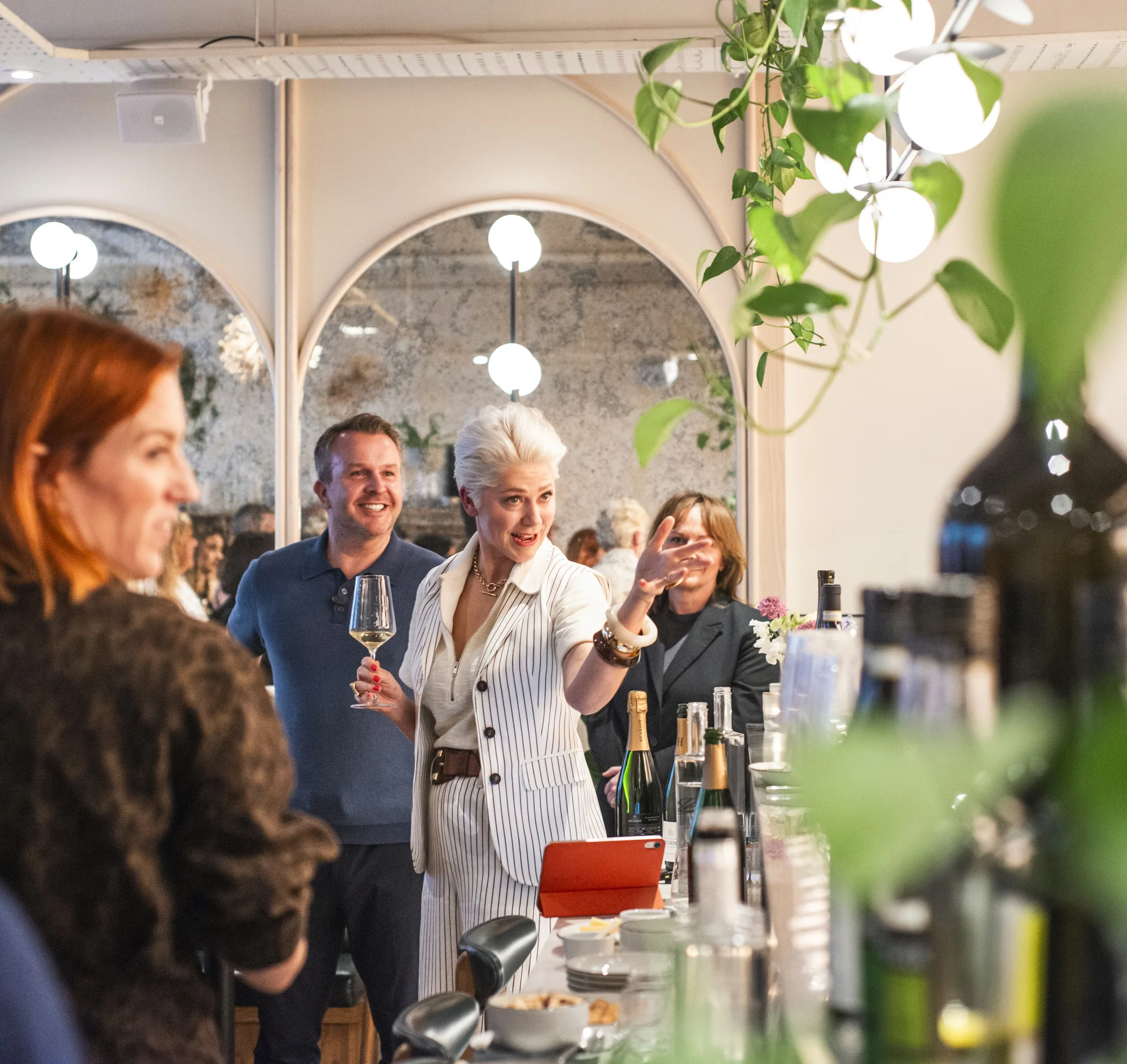Wine tasting guests gathered around a bar as a presenter holds a glass and speaks