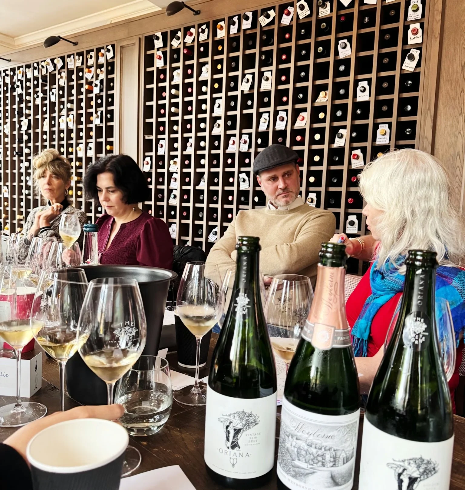 Guests tasting sparkling wine beside a wall of wine bottles