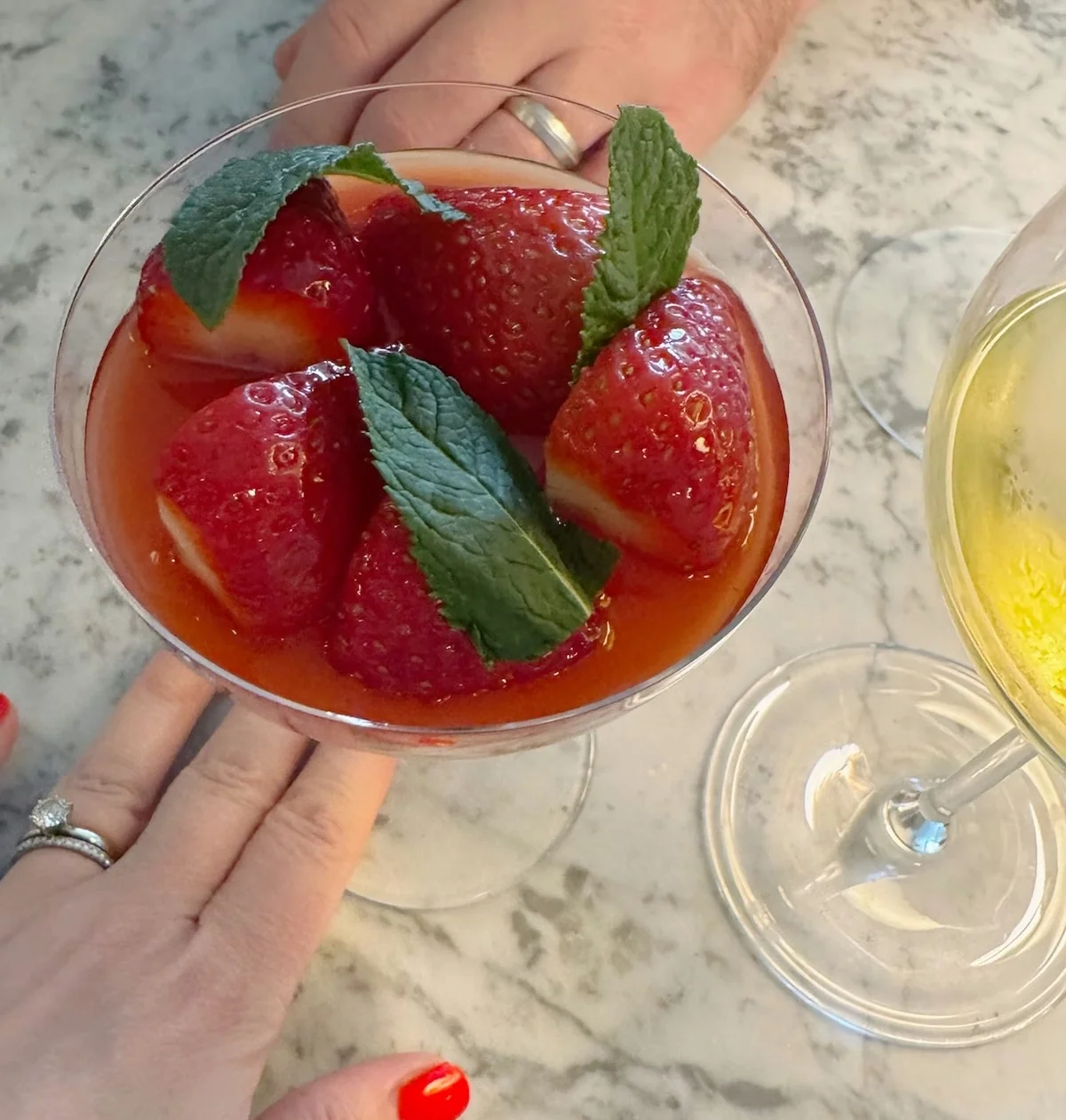 Strawberries and mint garnish a pink cocktail beside a glass of pale wine