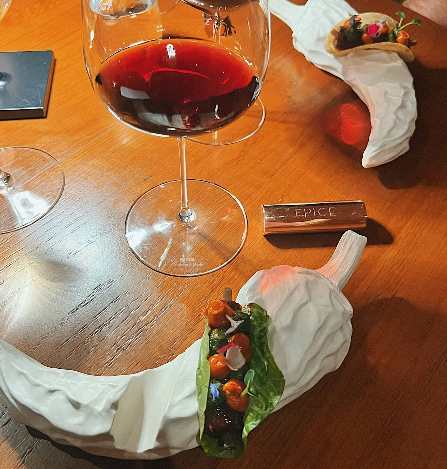Red wine in a labelled glass beside artistic small plates at EPICE