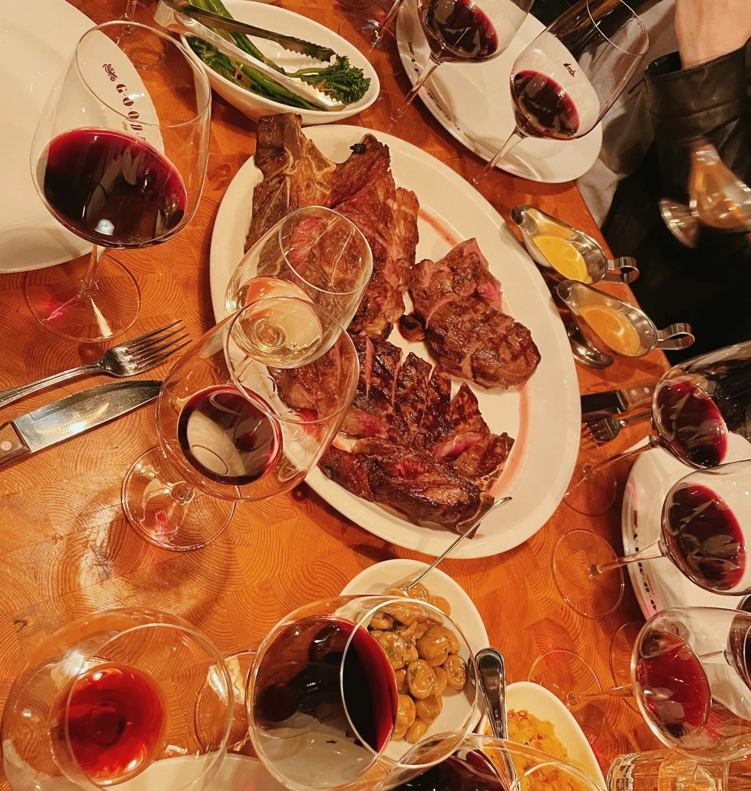 Argentine-style steak dinner surrounded by red wine glasses and side dishes