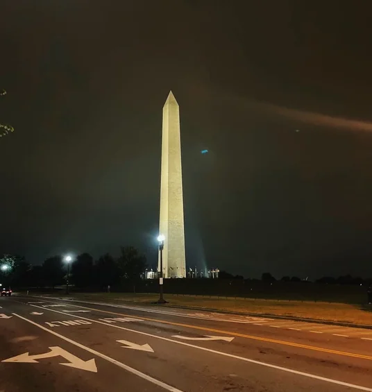 Illuminated obelisk beside a marked road at night