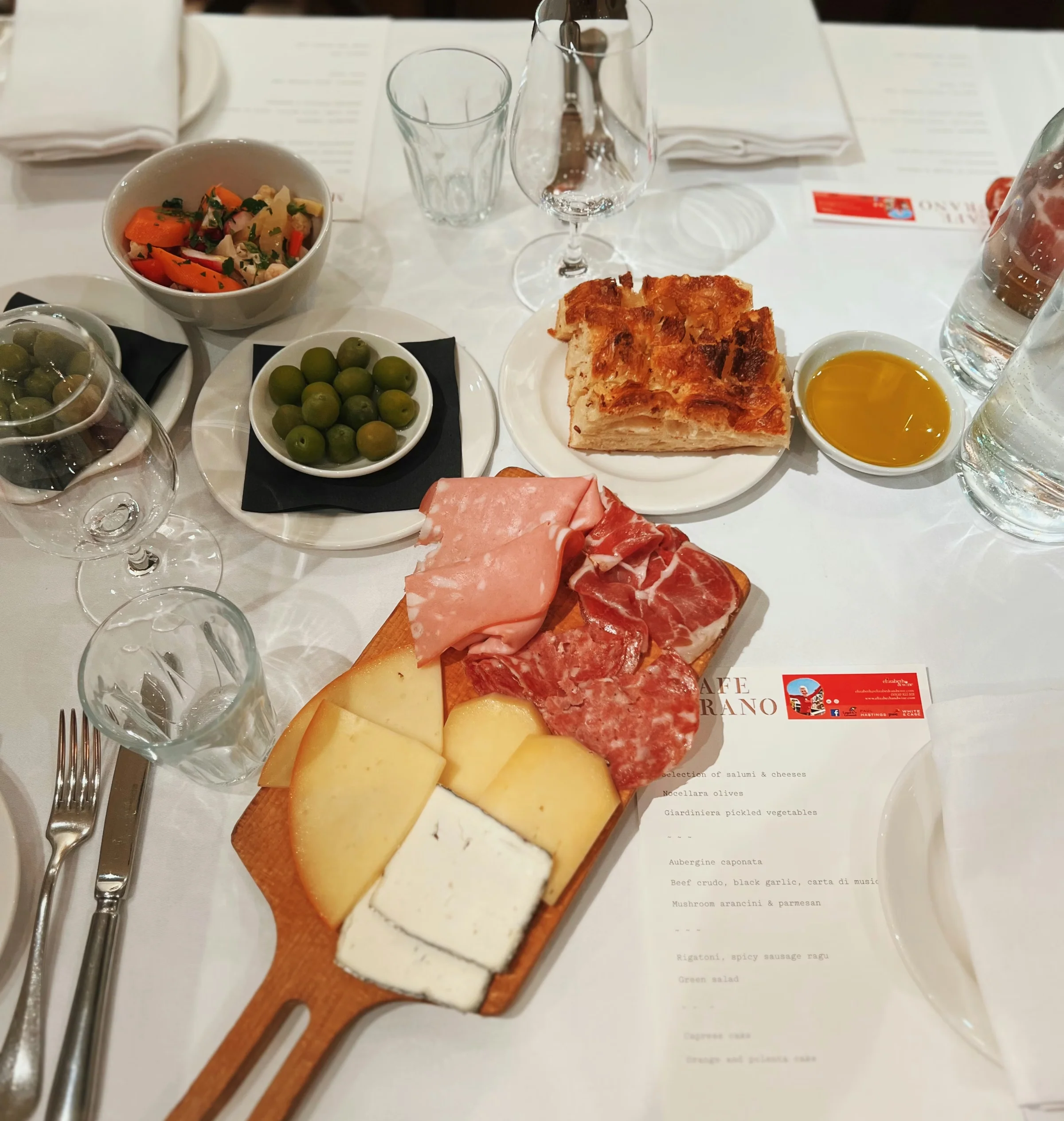 Italian-style restaurant table with wine glasses, antipasti, bread, olives and a printed menu