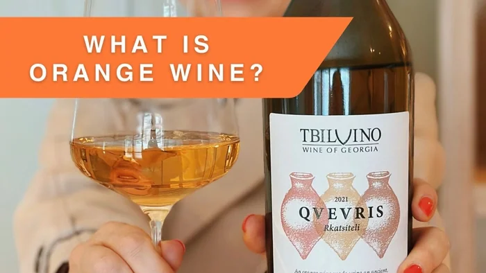 Orange wine bottle and glass held by person indoors