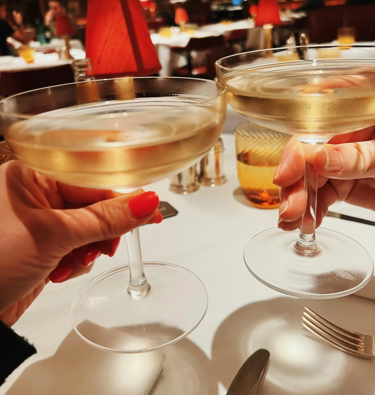 Two coupe glasses of pale sparkling wine held above a restaurant table