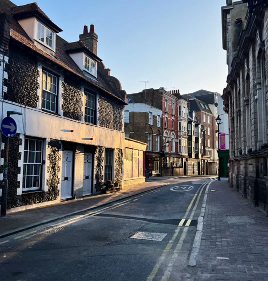 Sunlit historic street in Margate with flint-faced buildings and a church wall