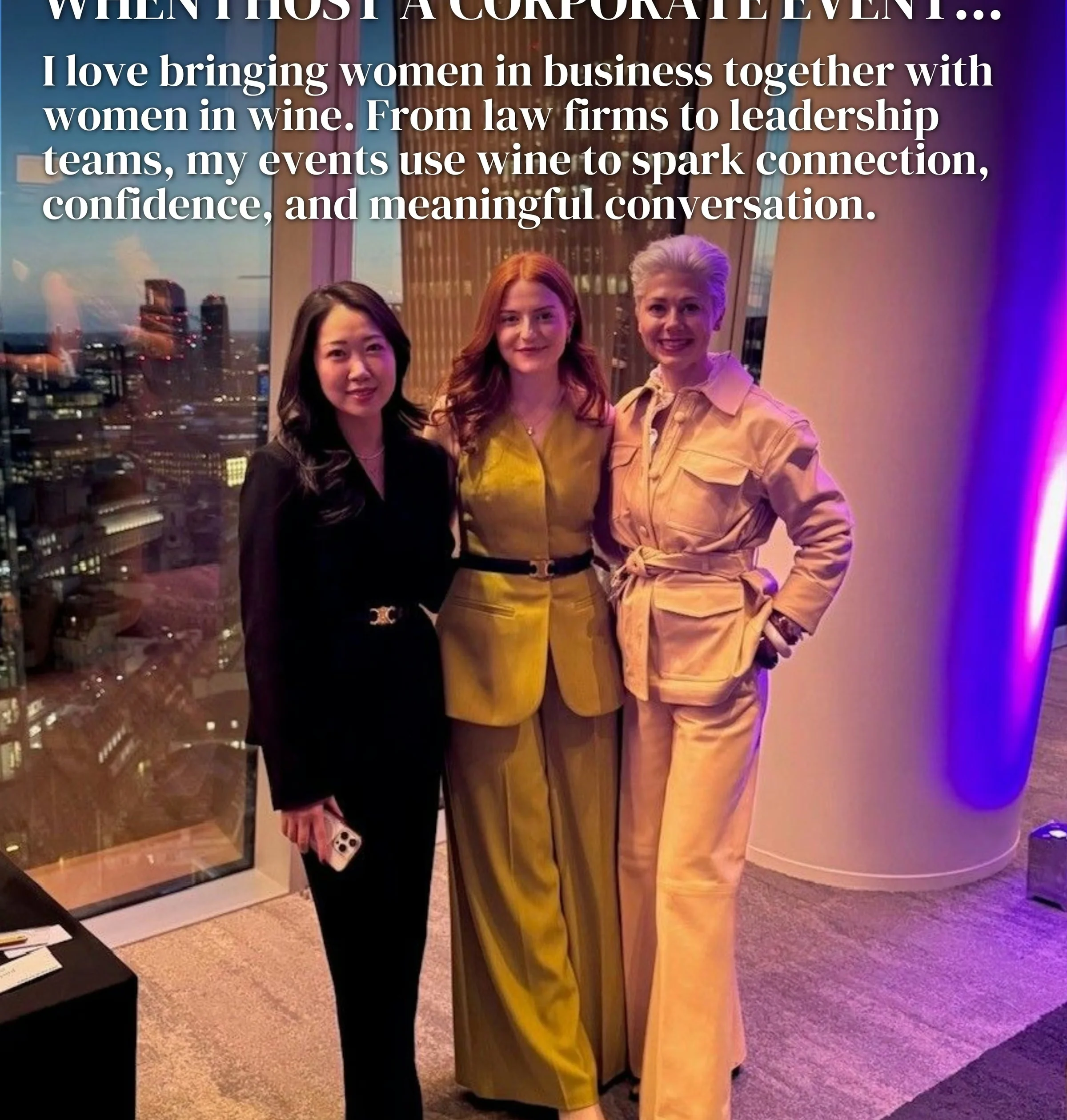 Three women pose at a corporate event beside a window overlooking the city