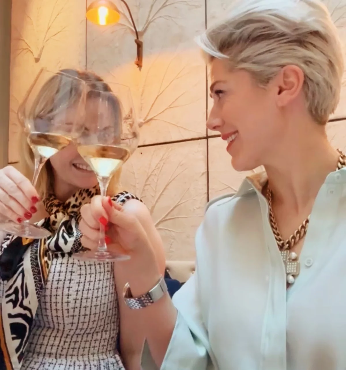 Two women clink glasses of rosé at a restaurant table, with a pink dessert in the foreground.