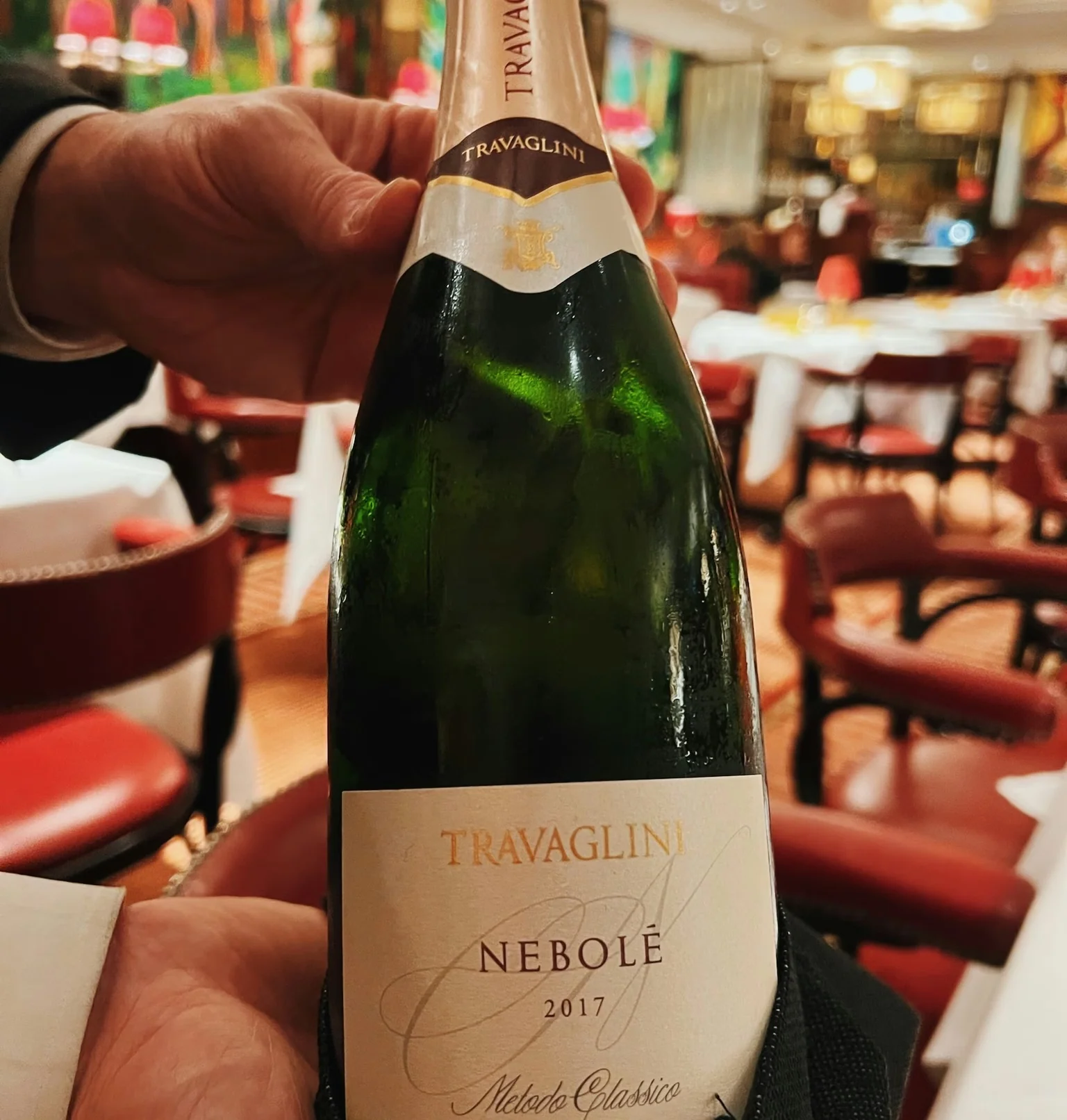 Travaglini Nebolè 2017 sparkling wine bottle held in a colourful restaurant