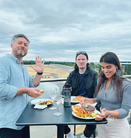 Three people enjoying food and wine beside a racetrack at Mercedes-Benz World
