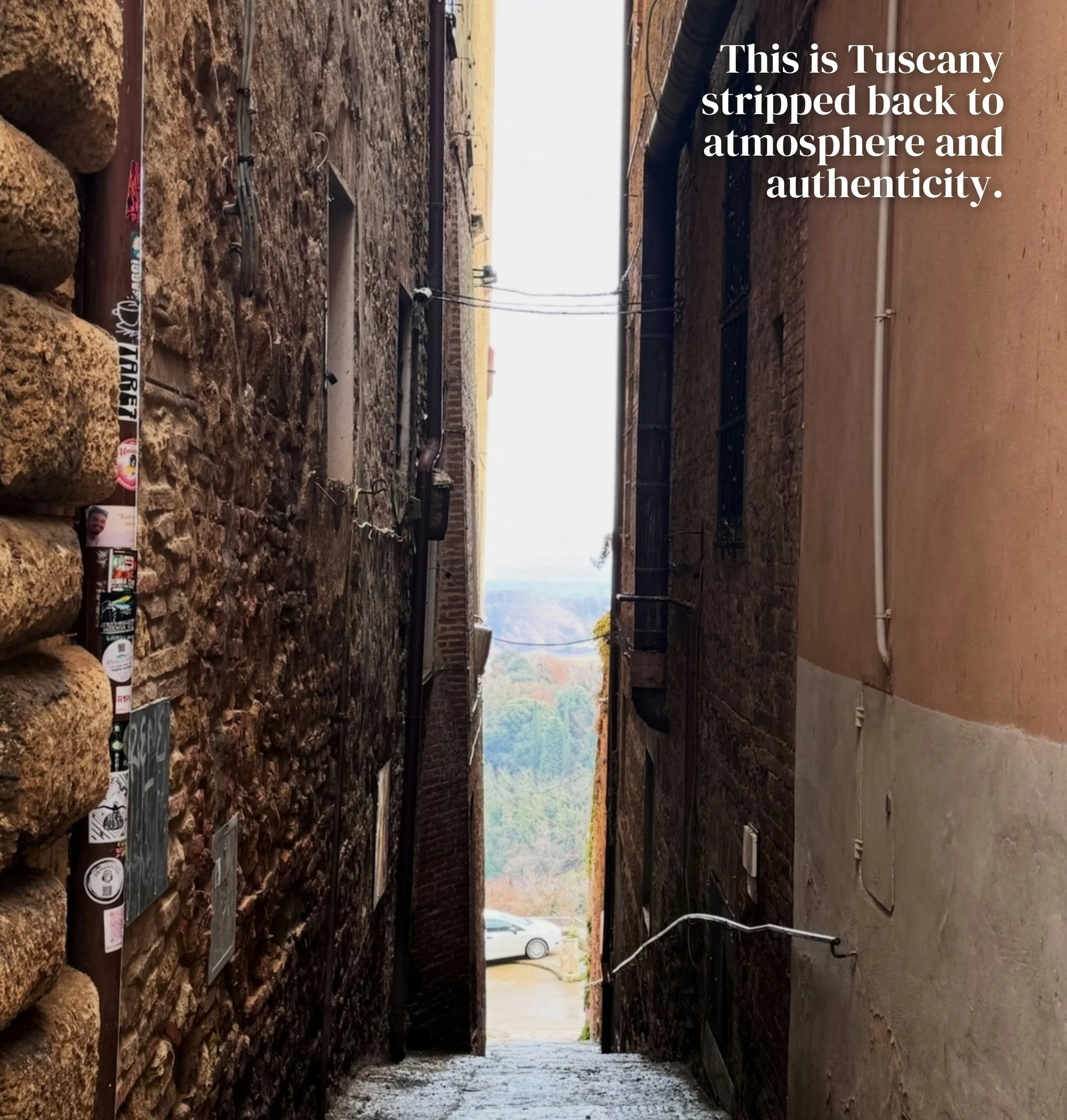 Narrow stone alley opening onto a wooded Tuscan valley