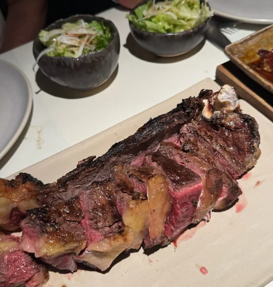 Sliced grilled steak, pink in the centre, served on a platter with bowls of green salad